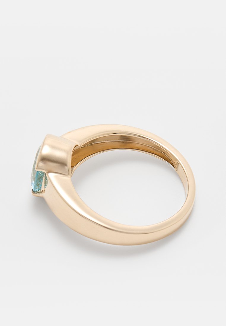 Goldring mit einem glatten, abgerundeten Band und einem auffälligen hellblauen Stein, der schräg eingesetzt ist. Polierte Oberfläche, modernes Design.