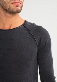 Maglietta a maniche lunghe grigio scuro a trama con scollatura rotonda e maniche raglan, caratterizzata da cuciture precise lungo le cuciture.