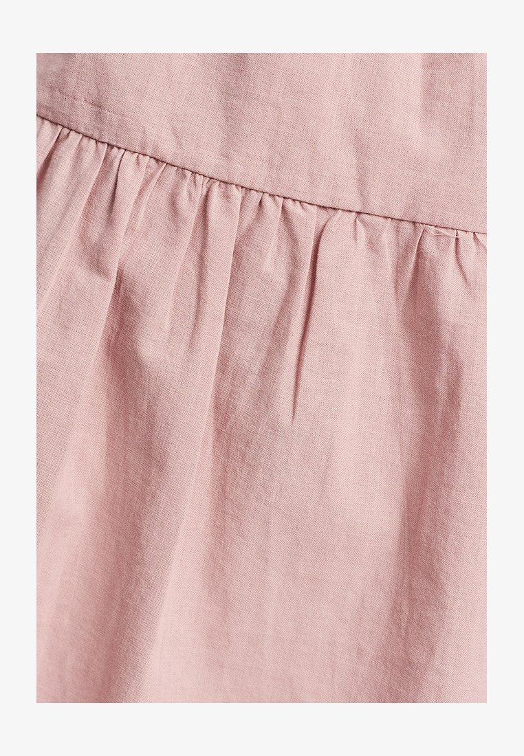 Svetloružová látka s jemnou textúrou, s nahrnutými detailmi v oblasti pása a jemnými vráskami, ktoré vytvárajú hĺbku v dizajne.