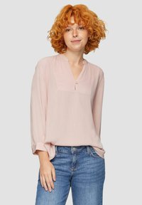 Lichtroze blouse met lange mouwen en een knoopsluiting in V-vorm, met subtiele textuur en een borstzakje. Gepaard met denim jeans.