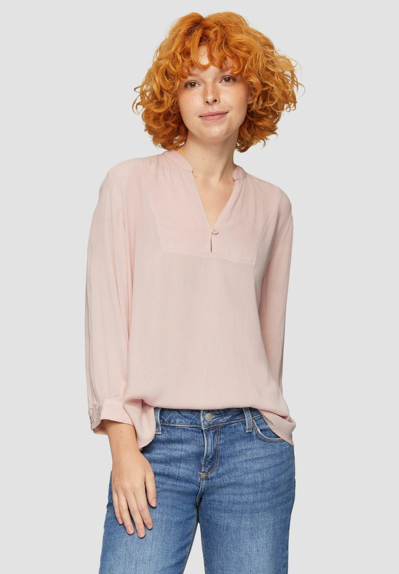 Lichtroze blouse met lange mouwen en een knoopsluiting in V-vorm, met subtiele textuur en een borstzakje. Gepaard met denim jeans.