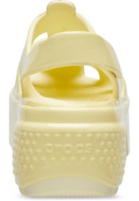 Żółte plastikowe sandały na platformie z tylnym wycięciem i teksturowaną podeszwą z małymi bąbelkami. Design paska oferuje otwarty styl.