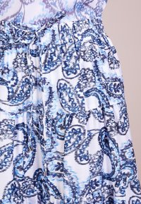 Jupe en tissu blanc avec un motif cachemire bleu et marine, taille élastique avec un cordon de serrage, et volants superposés le long de l'ourlet.