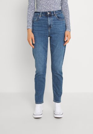 Jean en denim bleu clair avec taille haute, coupe slim, design à cinq poches et coutures visibles, associés à des baskets blanches.