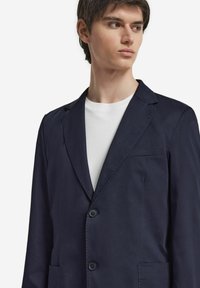 Marinblå blazer med en elegant design, som har slagna kragar, två knappar och en enda bröstficka. Lättviktig tyg med en jämn textur.