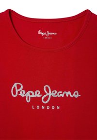 Raudonas medvilninis marškinėlis su apvaliu kaklu, ant kurio priekyje yra sidabrinės blizgučiais užrašytas tekstas "Pepe Jeans LONDON". Lygus audinys, kasdieniškas dizainas.