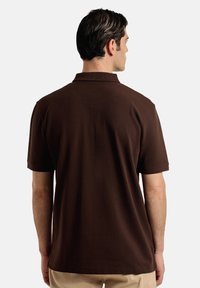 Polo marrón con cuello clásico, mangas cortas y dobladillo recto. Material de algodón suave con una textura lisa y sin patrones visibles.