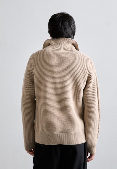 Beige ribbed knit sweater with a high collar, features long sleeves and a relaxed fit. Smooth texture, minimal design, and no visible patterns.
