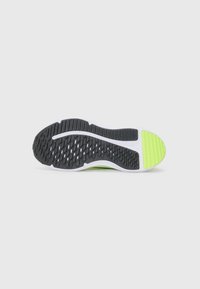Semelle de chaussure en caoutchouc noir avec un motif de grip texturé, bande de semelle intermédiaire blanche, et un accent vert vif près du talon.