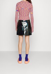 Haut à manches longues coloré et à motifs associé à une jupe en vinyle noir brillant. Porté avec des sabots orange et des chaussettes côtelées violettes.