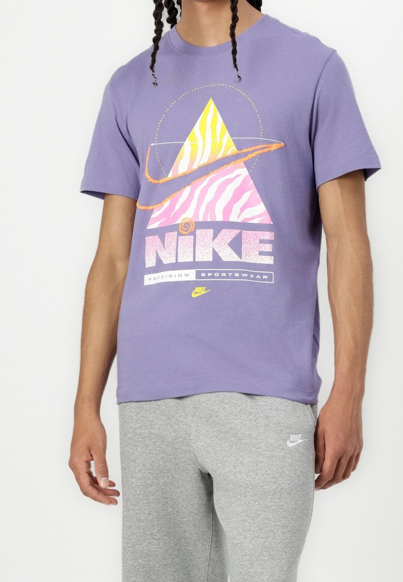 Camiseta de algodón morada con un diseño gráfico colorido que presenta un patrón de zigzag, acentuado por el texto "Nike" y "Precision Sportswear."