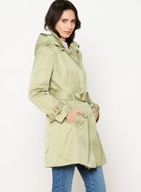 Trench coat impermeable de color verde claro con capucha, cintura ceñida, grandes bolsillos y acentos en tono dorado. Textura lisa y brillante.