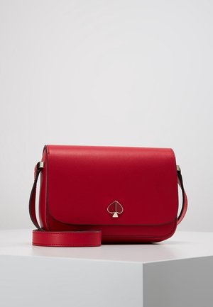 Czerwona skórzana torebka na ramię z klapką, cienkim regulowanym paskiem oraz małym srebrnym logo w kształcie karo na przodzie, przedstawiona na białym tle.