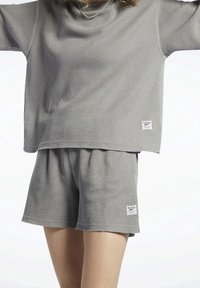Šedá žebrovaná relaxační souprava obsahující top s krátkým rukávem a šortky. Materiál má měkkou strukturu. Obsahuje malou značkovou etiketu na každém kusu.