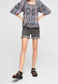 Mönstrad blus i flera färger med puffärmar, kombinerad med uppvikt grå denimshorts och svarta platta sandaler. Avslappnad sommaroutfit.