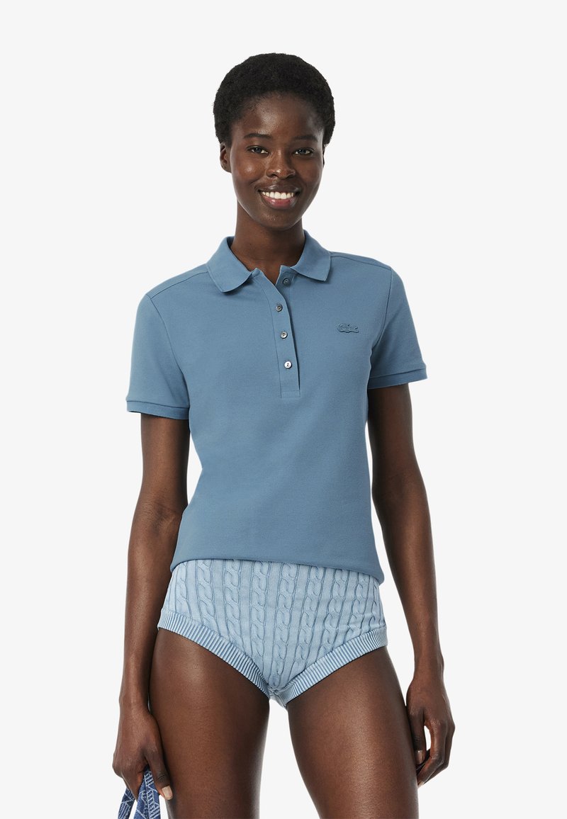 Ljusblå piké med krage, fyra knappslå och diskret logotyp. Bärs med mönstrade ljusblå shorts med kabelstickad design.