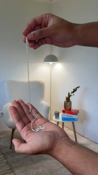 Corrente de prata segurada numa mão, com elos entrelaçados. Fundo suave e texturizado com uma cadeira, uma lâmpada e livros na cena.