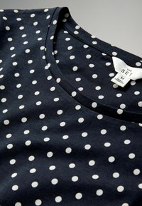 Donkerblauwe katoenen T-shirt met witte stippen, met een V-hals en een label met merk- en maatinformatie.