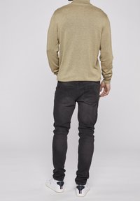 Maglione beige con collo alto e texture a coste, abbinato a jeans scuri e sneakers bianche con dettagli neri. Visto da dietro.