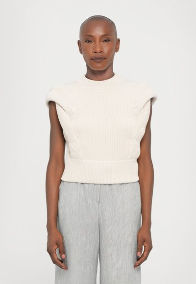 Strikket kreamfarvet ærmeløs sweater med ribbet tekstur og struktureret skulderdesign, parret med lyse stribede vidde bukser.