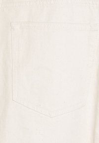 Detailní záběr jednoduché bílé látkové kapsy s viditelným šitím na světlém textilním pozadí.