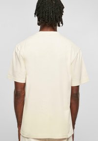 Tricou din bumbac de culoare crem, cu o croială clasică, mâneci scurte și decolteu rotund, având o textură fină și un design minimalist.