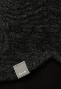 Bonnet en tricot noir avec une texture douce. Présente une étiquette rectangulaire grise avec le logo "Bench." L'ourlet est légèrement courbé.