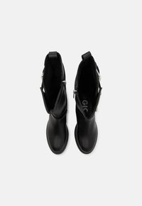 Botas de tobillo de cuero negro con un acabado suave, que cuentan con cremalleras laterales y tiradores. El interior muestra un forro suave con el logotipo de la marca.