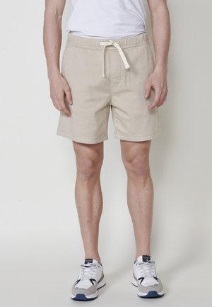Pantaloni scurți din bumbac bej, cu bandă elastică la talie, șnur și buzunare laterale. Croi clasic, cu un design simplu, asortați cu adidași albi.