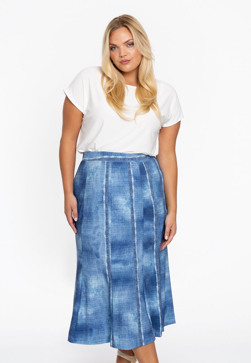 Jupe maxi en denim avec un délavage bleu, présentant des coutures verticales. Associée à un haut blanc uni à manches courtes.