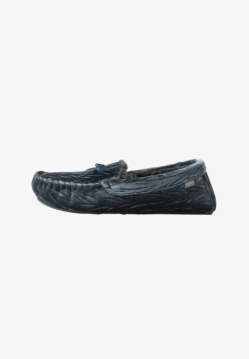 Pantofole moccasin in velluto nero con dettagli cuciti, morbido rivestimento in pelliccia, un fiocco decorativo e suola in gomma piatta per comfort e aderenza.