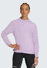 Lys lilla zip-up jakke med hætte, lavet af glat stof. Har lange ærmer og et subtilt logo på brystet.