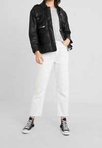 Černá kožená bunda s límcem, několika předními kapsami a upnutým střihem. Kombinována s bílými džínami s širokými nohavicemi a černými vysokými teniskami.