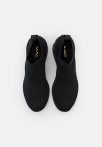 Baskets noires à enfiler en tricot avec motifs texturés, languettes au talon et logo ALDO visible à l'intérieur des chaussures.