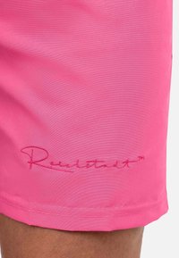 Shorts de bain roses en tissu lisse, avec un logo brodé en rose plus foncé à l'ourlet. Design simple sans motifs ni accents.