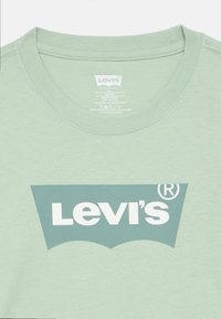 Ανοιχτό πράσινο βαμβακερό μπλουζάκι με στρογγυλή λαιμόκοψη, με μεγάλο λευκό λογότυπο Levi's και σχέδιο νυχτερίδας στο μπροστινό μέρος.