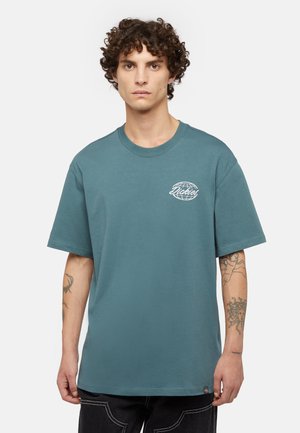 T-shirt en coton teal avec un col rond et des manches courtes ; présente un logo imprimé en blanc sur la poitrine gauche et une petite étiquette de marque à l'ourlet.
