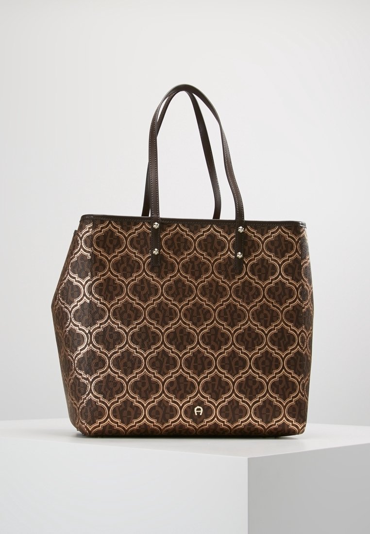 Brązowa torba typu tote wykonana z fakturowanego materiału syntetycznego, z geometrycznym wzorem w ciemniejszych odcieniach, wyposażona w dwa solidne uchwyty i metalowe akcenty.