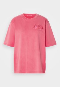 Rosa bomulls oversized T-skjorte med korte ermer, rund hals og et subtilt grafisk trykk på venstre brystområde. Glatt tekstur.