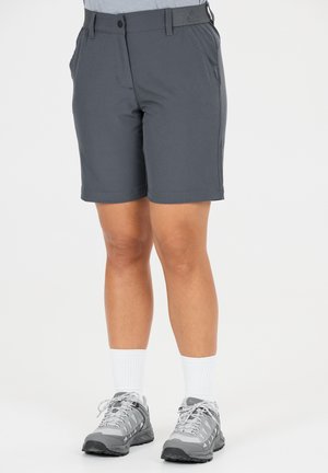 Jambes portant un short gris foncé jusqu'aux genoux, des chaussettes blanches montantes et des chaussures de sport grises sur un fond blanc.