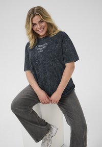 Black tie-dye T-shirt with "ATHLETIC" print, paired with gray flared pants and beige sneakers. The outfit features a relaxed, casual design.