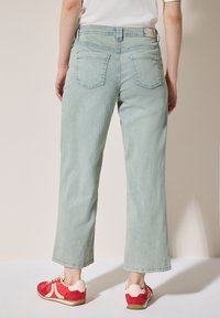 Ljusgröna vida jeans med en subtil tvätt, fem fickor och midja i normalhöjd, i kombination med röda och rosa sneakers.