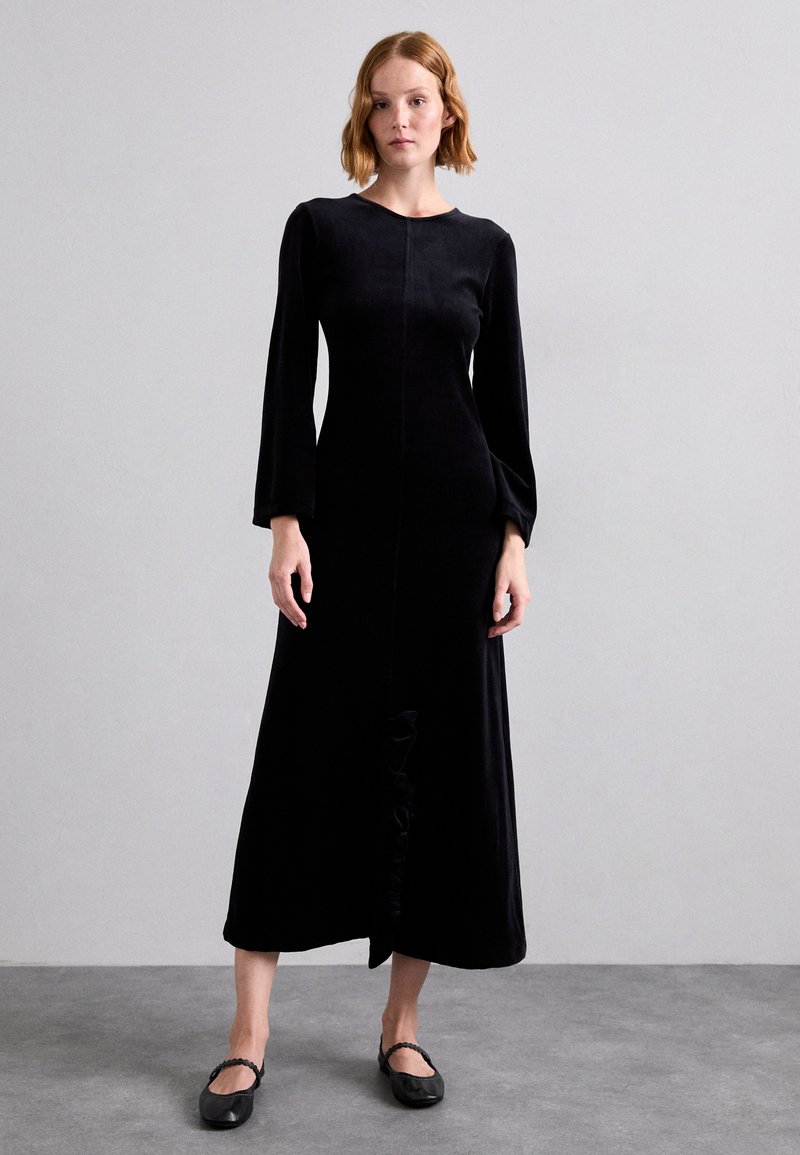 Black velvet dress with a round neckline, long bell sleeves, and a central seam. Features a gathered detail at the front hem.