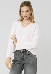 Pull à col en V rose clair en tricot doux, avec des manches longues et des bords côtelés, associé à un jean gris taille haute.
