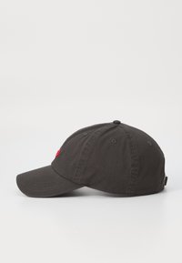Svart bomullsbasketcap med buet skygge, med rødt brodert logo foran, seks ventilasjonshull og justerbar stropp bak.