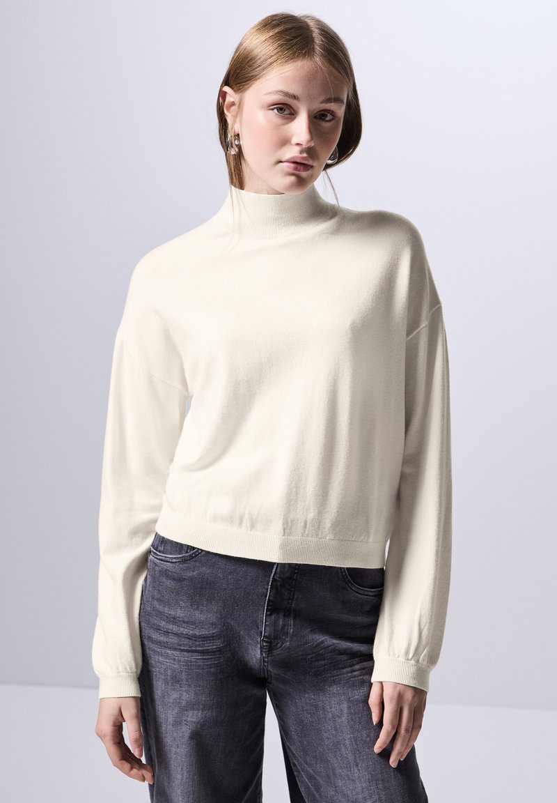 Maglione a maniche lunghe a collo alto, tagliato, in morbido tessuto crema. Presenta orlo e polsini a coste. Abbinato a jeans grigi scuri, dalla vestibilità comoda.