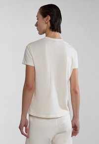 Lichtcrème T-shirt met korte mouwen, ronde hals en een zachte textuur. Naaddetails bij de hals; gestyled met bijpassende lichte broek.