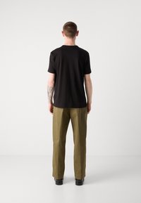Black cotton T-shirt with short sleeves, paired with olive green trousers and black shoes, viewed from the back against a plain background.