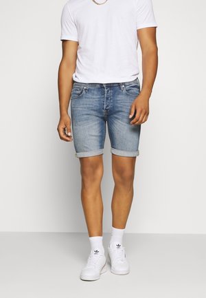 Jasnoniebieskie szorty dżinsowe z podwiniętymi mankietami, w połączeniu z prostą białą koszulką i białymi sneakersami. Posiadają delikatne przetarcia i tylne kieszenie.