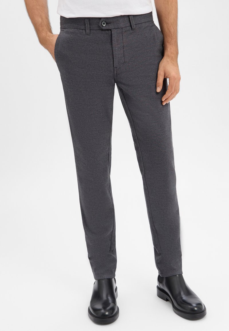 Grau maßgeschneiderte Hose mit strukturiertem Muster, flacher Vorderseite und Seitentaschen. Kombiniert mit schwarzen Stiefeletten; verfügt über einen einzelnen Knopf vorne.